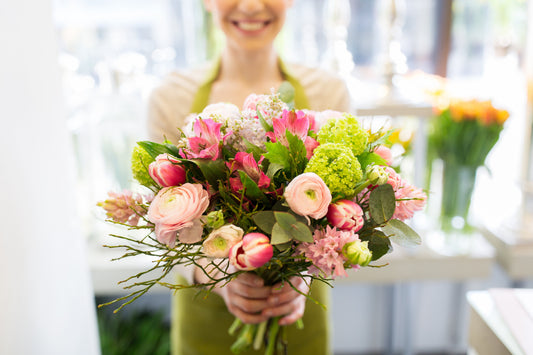 Florist holding a fresh mixed bouquet with roses, ranunculus, and greenery in flower shop