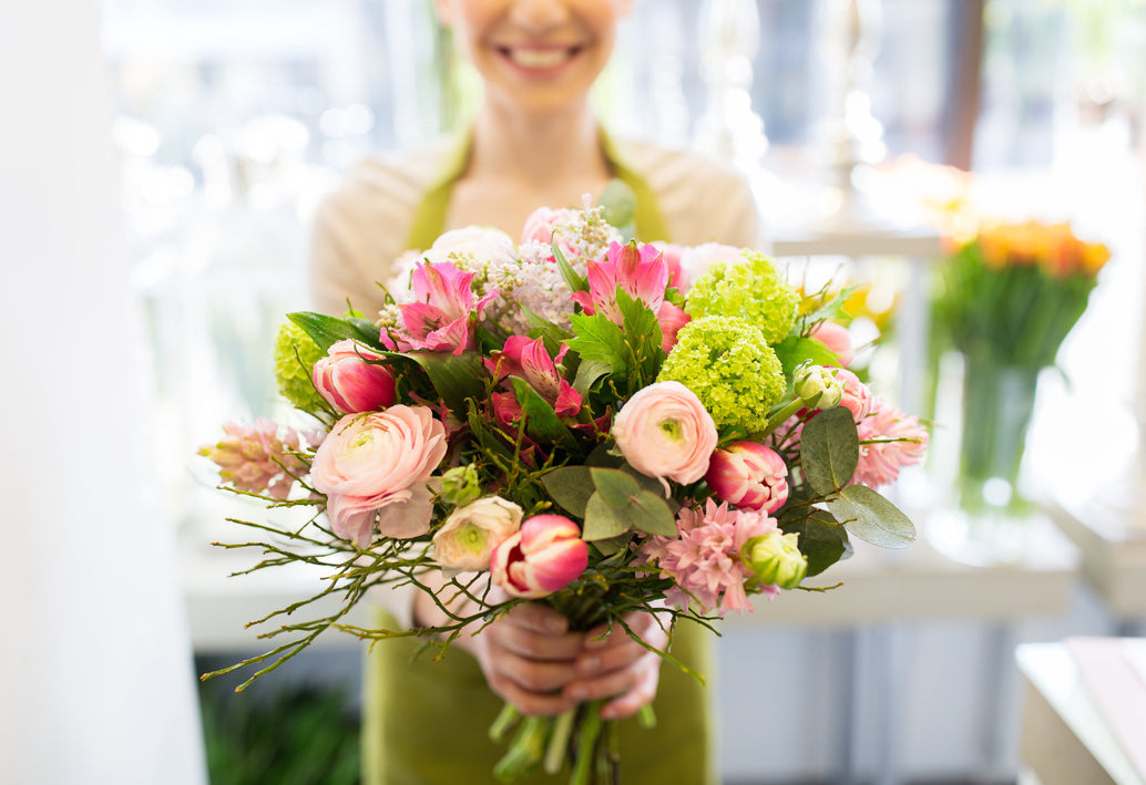Florist holding a fresh mixed bouquet with roses, ranunculus, and greenery in flower shop