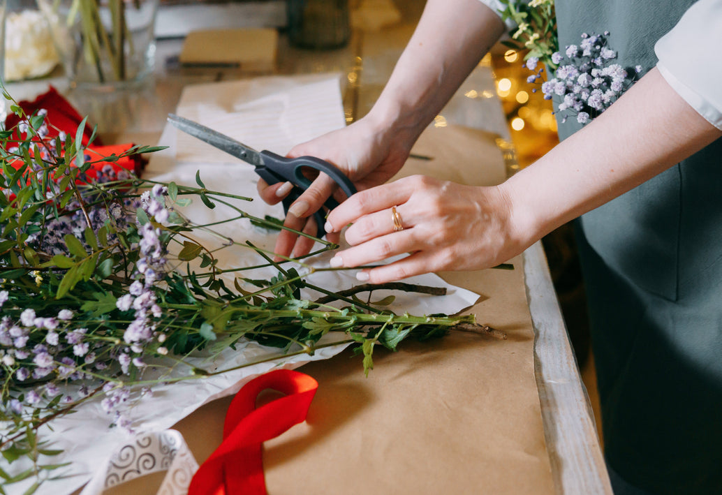 Florist trimming fresh flowers with scissors while arranging bouquet on worktable, classic floral design preparation in studio
