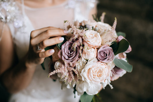 Bride holding a bouquet of blush, ivory, and lavender roses with soft greenery and delicate accent flowers