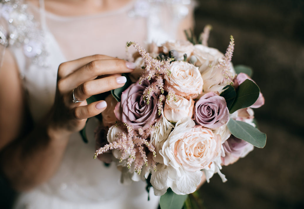 Bride holding a bouquet of blush, ivory, and lavender roses with soft greenery and delicate accent flowers