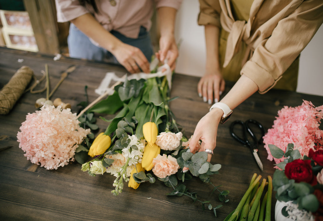 Florists arranging a designer-level bouquet with tulips, hydrangea, roses, and eucalyptus on a wooden table