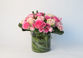 A modern floral arrangement of pink and white roses in a clear glass vase with woven greenery, styled by Allan Woods Flowers.