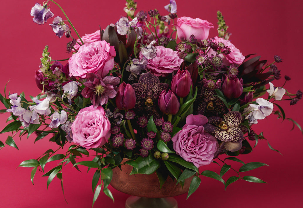 A romantic blend of soft pinks and rich berry tones creates a timeless expression of love. Nicole is an elegant, garden-style arrangement featuring lush roses, tulips, orchids, sweet peas, and seasonal blooms.